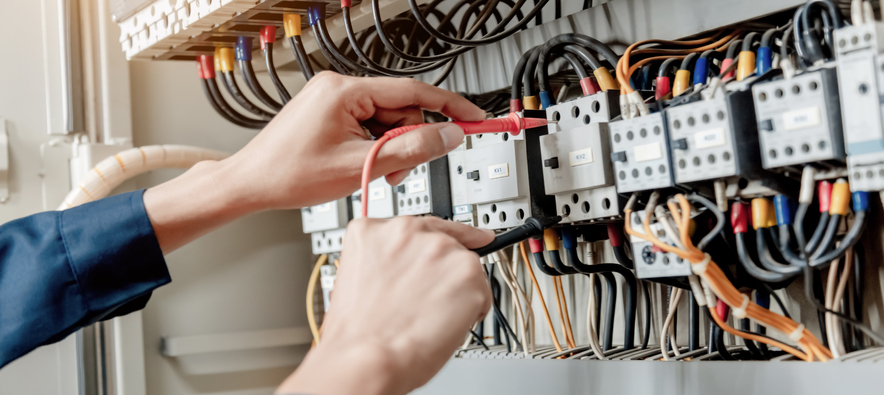 Electrician engineer uses a multimeter to test the electrical installation and power line current in an electrical system control cabinet.